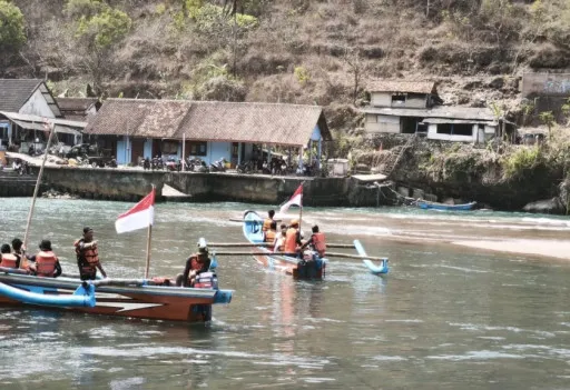 Wisatawan dan tim SAR melintasi sungai yang memisahkan kawasan pantai Baron 